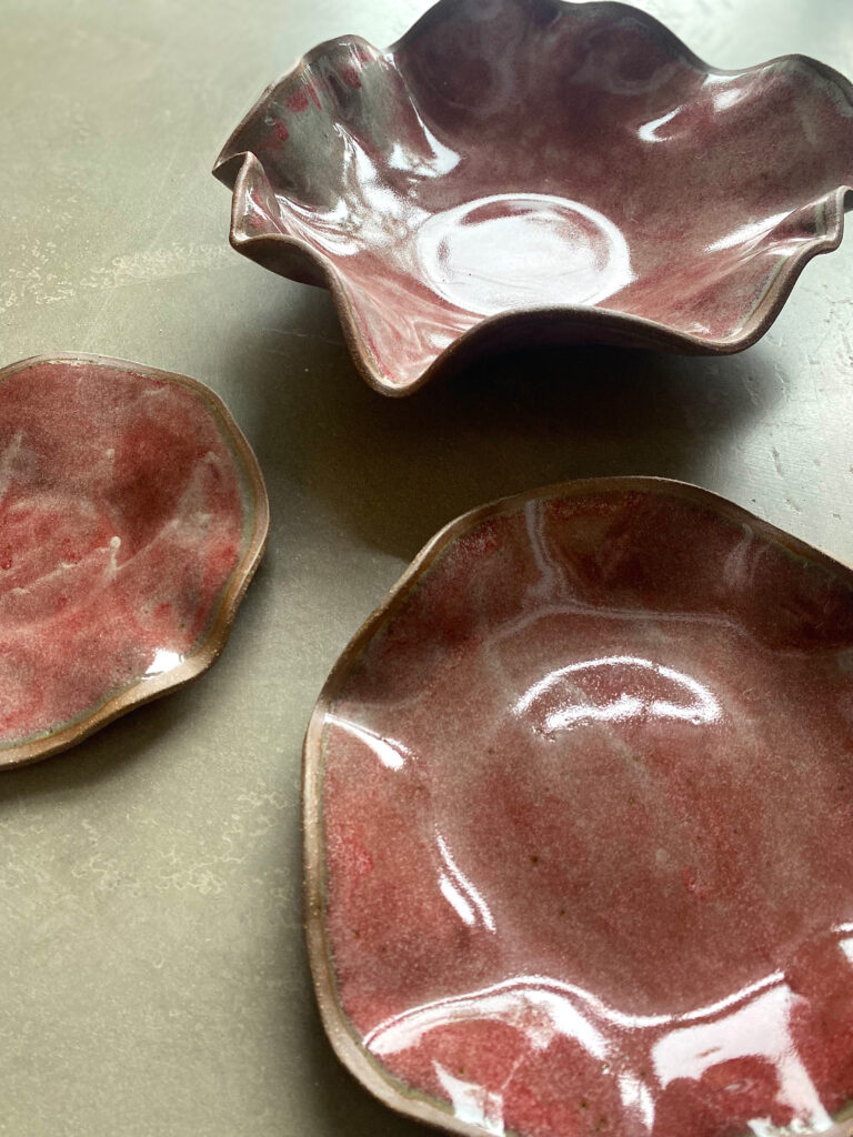 A group of three ceramic platters, each with a ruffled edge, a rustic red color and a shiny finish