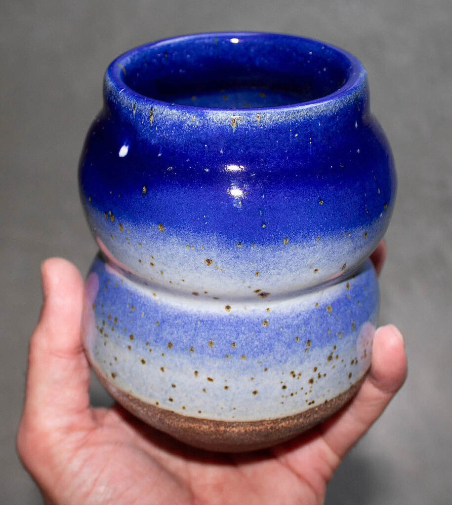 A hand seen holding a dark and light blue vase that has small specks of gold coloring along its surface