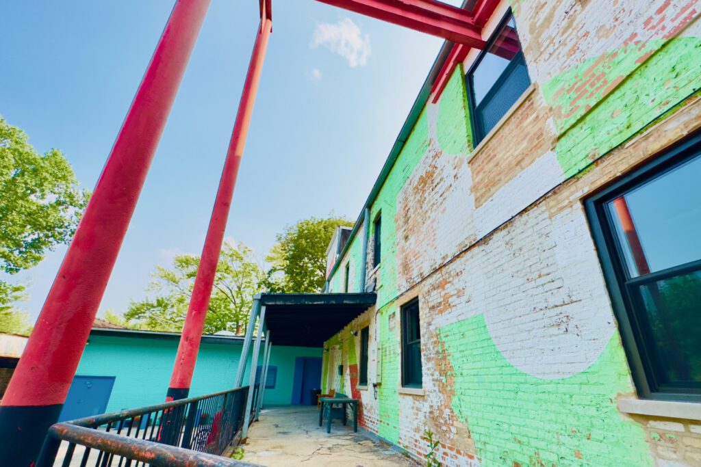 A brick building painted with bright white and bright green paint with large, red steel beams protruding out of the second story
