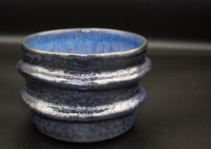 A naturalistic ceramic bowl with shiny, silver and blue patina coloring