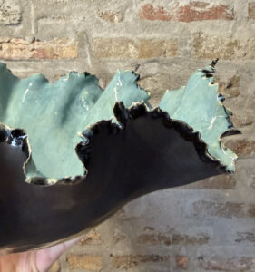 A ceramic bowl sculpture with edges resembling a leafy vegetable has a shiny, bright green surface