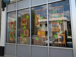 A window display of various insects arranged on wood-slat panels. Each panel is nearly floor to ceiling height and include small wooden leaf pieces in various colors