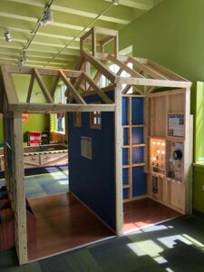 A museum exhibition which is made to look like the wood frame of a building with some electrical equipment an indicator bulbs visible on a panel