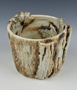 A light ceramic cup with natural textures and colors like tree bark and leaf shapes attached to its side